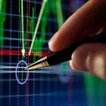 Une main et un stylo sur courbe de trading